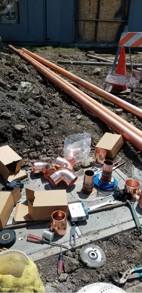 Copper pipe and fittings staged at an excavation for a new water service line